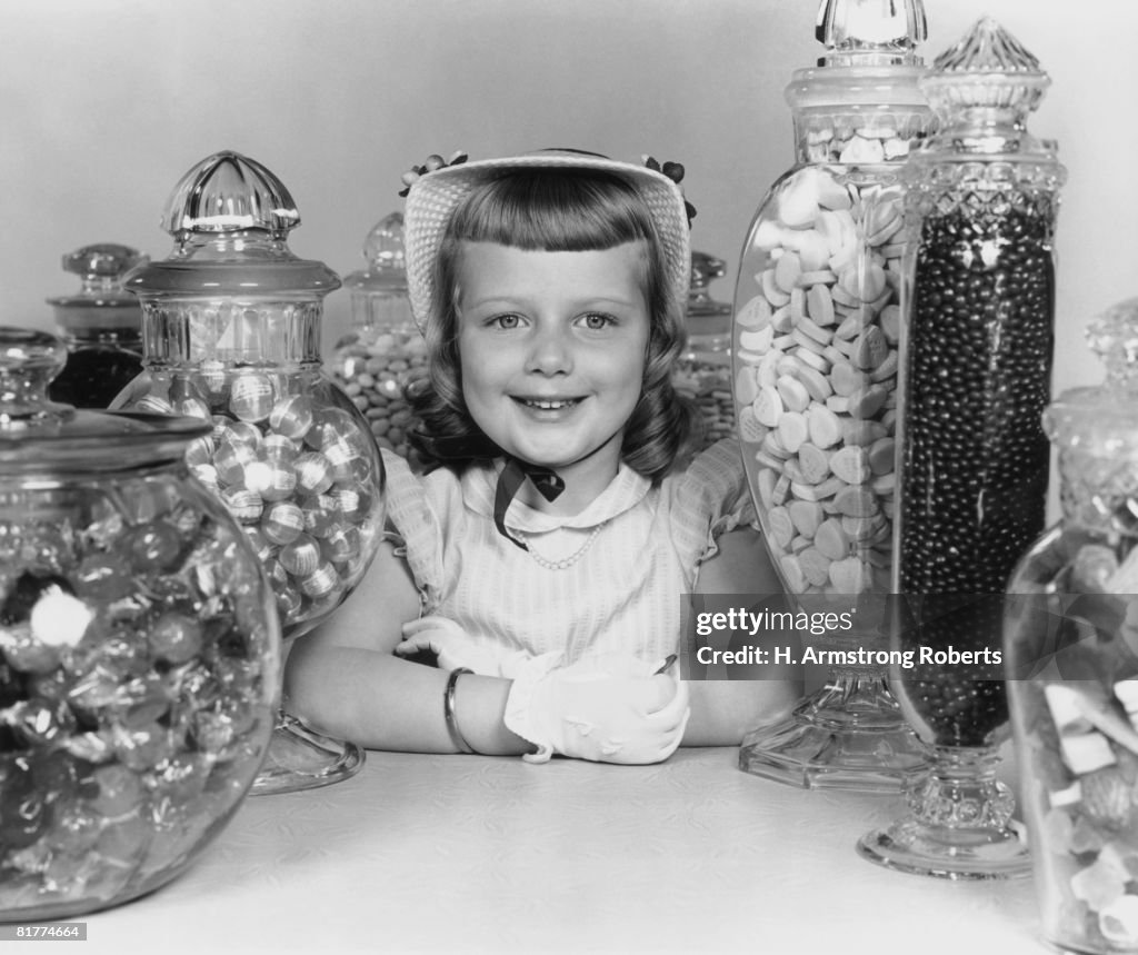 Girl wearing hat and gloves with candy jars.