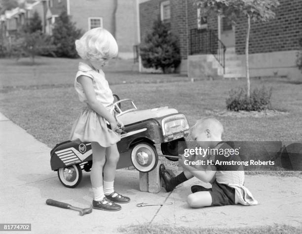 children on suburban sidewalk, boy playing as mechanic, oiling toy pedal car. - boy toy stockfoto's en -beelden