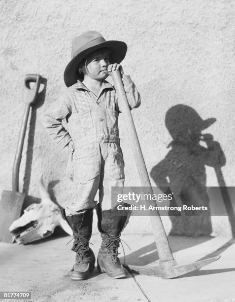 girl wearing overalls, holding pick and shovel, portrait. - 20th century stockfoto's en -beelden