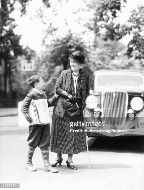 newsboy with stack of papers under arms, helping elderly woman with cane cross street. - grandma cane stock pictures, royalty-free photos & images