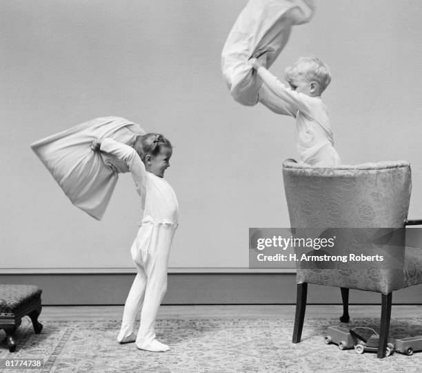 boy and girl having a pillow fight, boy standing on chair swinging pillow, girl on floor. - luta de almofada imagens e fotografias de stock