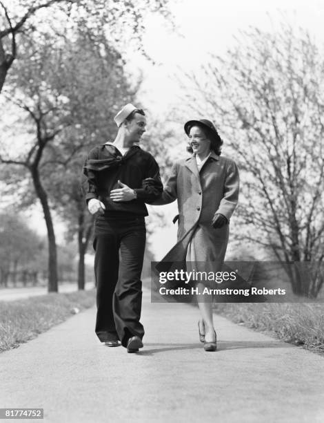 couple walking arm in arm outdoors, man wearing naval sailor uniform, woman wearing coat, hat and gloves. - 1940 stock pictures, royalty-free photos & images
