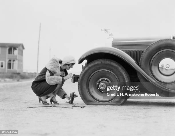 woman changing flat tire on car. - fotos años 20 fotografías e imágenes de stock