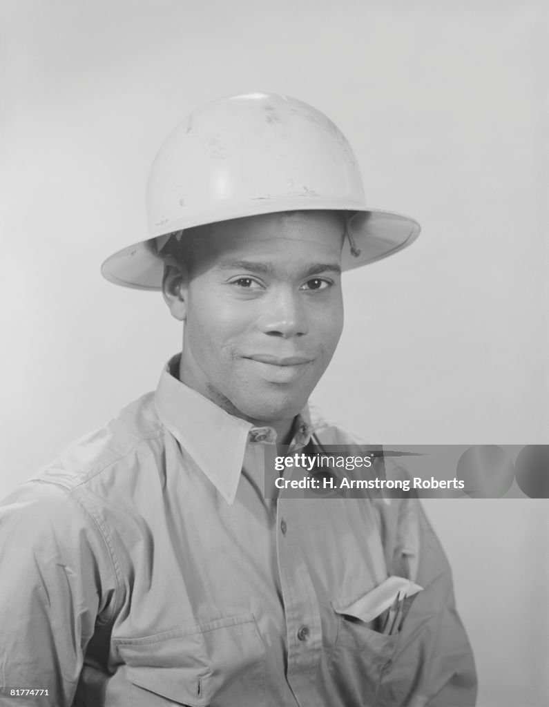 African-American man wearing work shirt and hard hat, portrait.