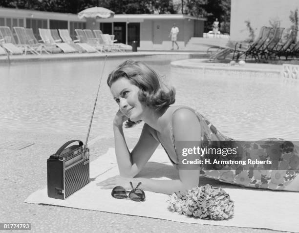 woman lying on towel poolside listening to radio with antenna up. - años 60 fotografías e imágenes de stock