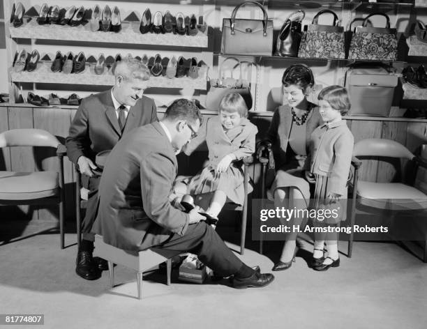 family of four in shoe shop, salesman fitting shoe on girl as mother, father and sister look on. - shoe shop assistant stock pictures, royalty-free photos & images