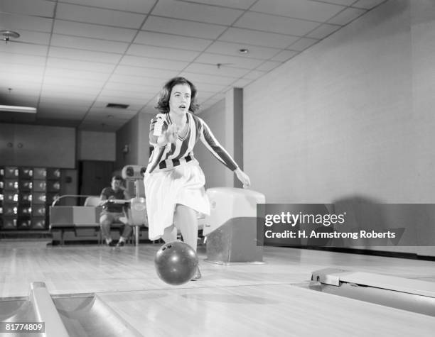 teenage girl releasing bowling ball into alley, friend looking on in background. - retro bowling alley stock pictures, royalty-free photos & images