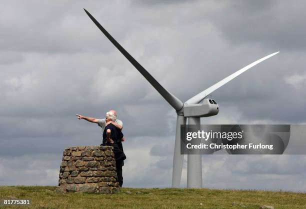 Couple of walkers stand by a cairn as they view the turbine sails of the controversial Scout Moor Wind Farm in the South Pennines, on June 30 in...