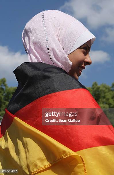 Young Muslim girl wearing a headscarve and a German flag waits for the German national football team to arrive at the Fan Mile in front of the...