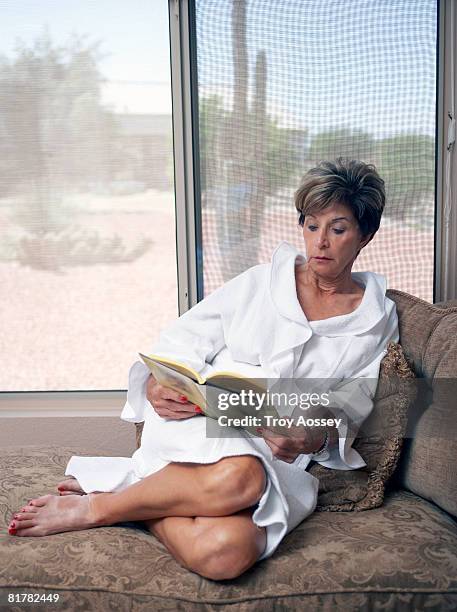 senior lady lounging in bath robereading book - surprise arizona stockfoto's en -beelden