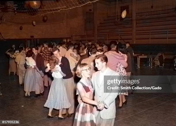 Young man and young woman hold hands and laugh together while slow dancing during a high school dance in the gymnasium at Monterey Union High School,...