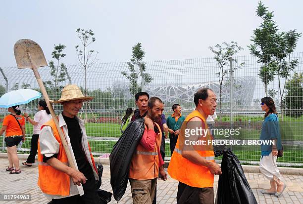 Construction workers walk past a fenced-off National Stadium, also known as the Birds Nest, which will host the opening and closing ceremonies as...