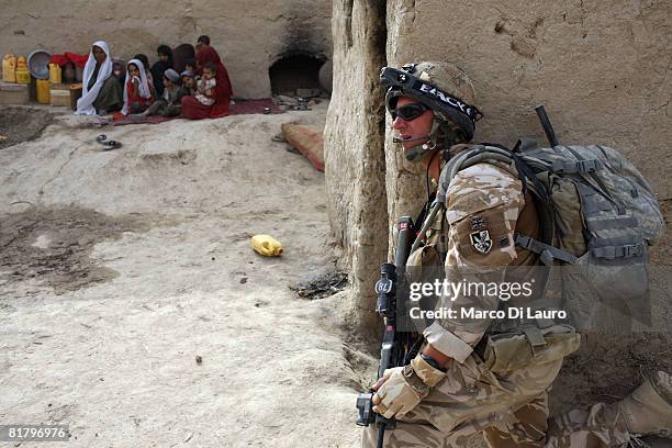 Afghan women and children sit in a compound as British Paratrooper from the 3rd Battalion The Parachute Regiment Pvt. Mark Pearce from Beckenham,...