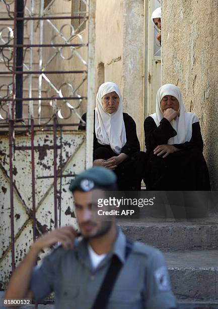 An Israeli border policeman stands near relatives of Hussam Tarysir Dwayat, the Palestinian bulldozer driver who executed an attack in Jerusalem, at...