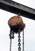 Antique rust of steel Hoist and steel chain hanging on the timber and white sky background.