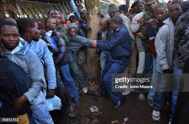 Policeman pulls a queue jumper out of a line of illegal Immigrants, most of them from Zimbabwe, at the entrance to a refugee center June 17, 2008 in...