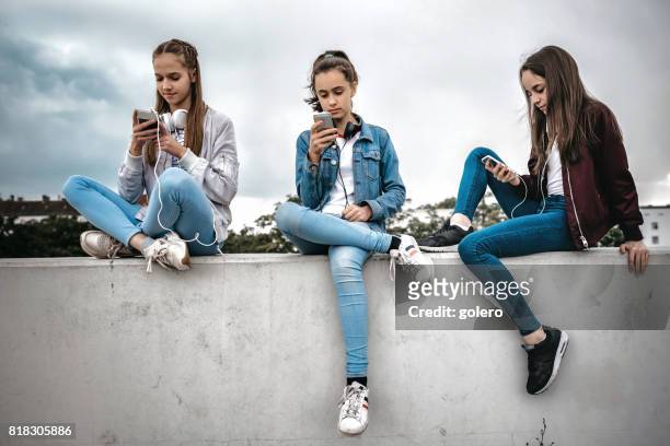 tre tonårstjejer med smartphones på betongvägg - girl mobile bildbanksfoton och bilder