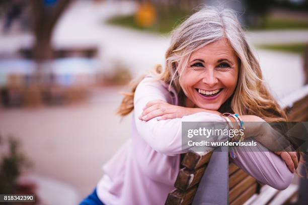 attractive senior woman laughing and sitting on park bench - wavy hair stock pictures, royalty-free photos & images