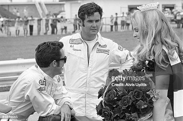Mario Andretti and Al Unser chat with the race queen before the start of the USAC INDY 150 Champ Car Race held on the road course at Indianapolis...