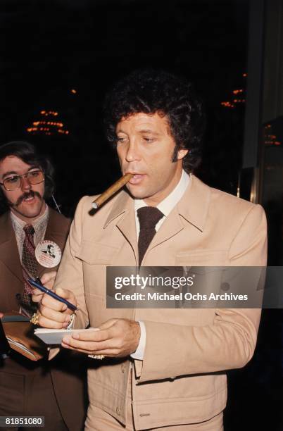 Welsh singer Tom Jones smokes a cigar and signs an autograph at the Friars Club Roast of George Raft, at the Beverly Hilton Hotel on February 6, 1975...