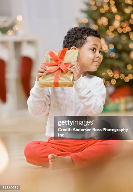 mixed race boy shaking christmas gift - gift excitement stock pictures, royalty-free photos & images