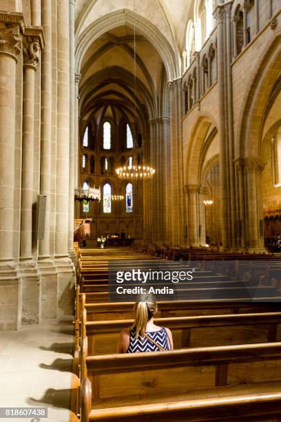 St Peter's Cathedral . Young woman seated alone a bench, praying.