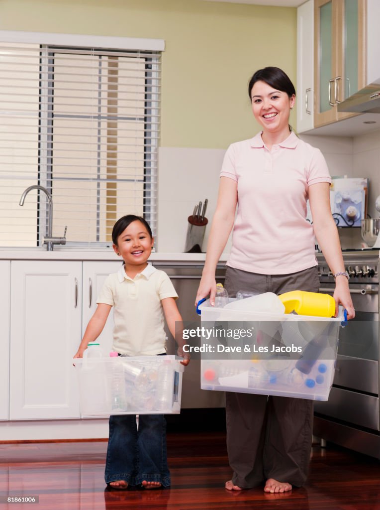 Mixed Race mother and daughter holding recycling bins