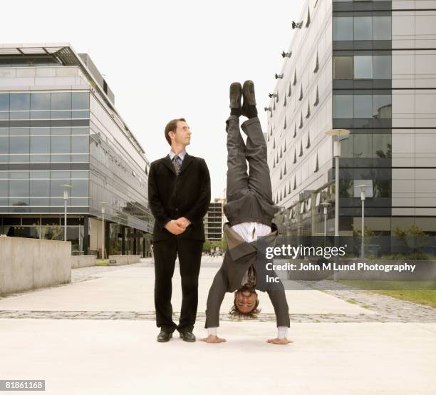 hispanic businessman doing handstand next to coworker - upside down stock pictures, royalty-free photos & images