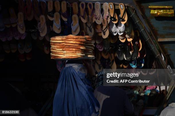 An Afghan woman carries breads for sale on her head early in the morning in Mazar-i-Sharif on July 19, 2017. / AFP PHOTO / FARSHAD USYAN