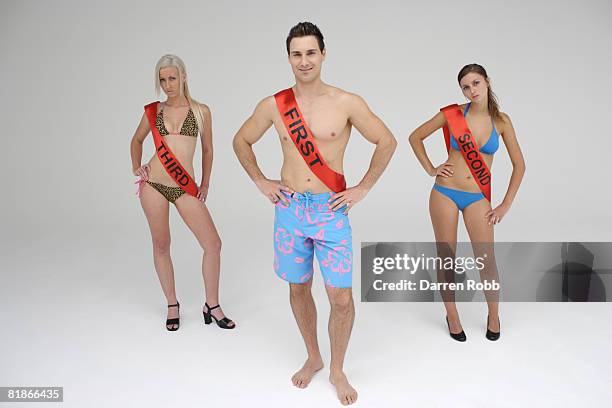 man wearing a first sash with two women wearing second and third looking miserable - beauty contest stock-fotos und bilder