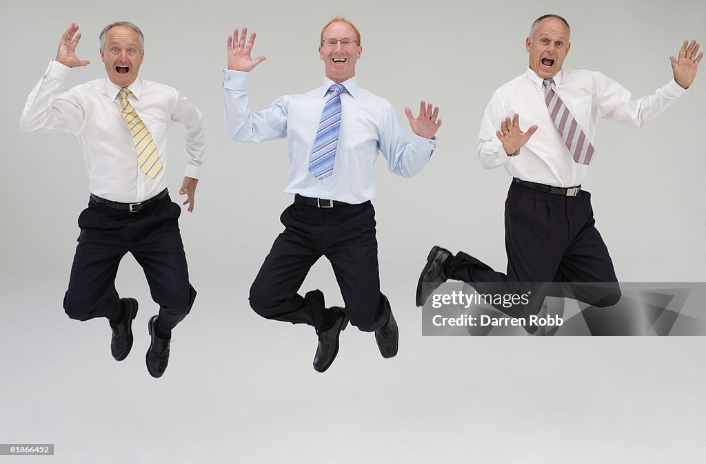 Three mature businessmen leaping in the air, laughing