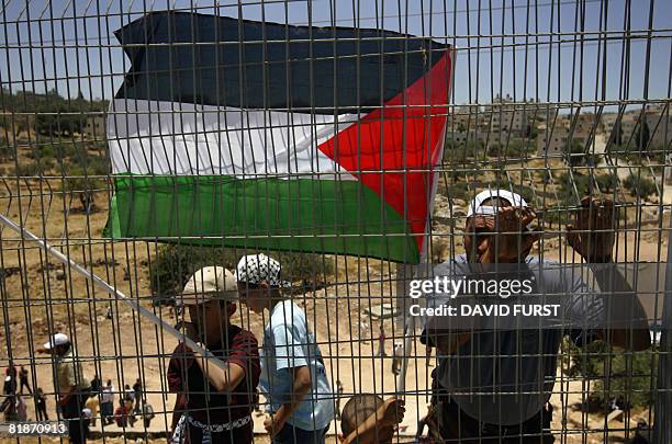 Palestinians demonstrators hold up their national flag along a fence separating them from a road used by Israeli vehicles during a protest marking...