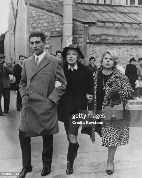 French singer Gilbert Bécaud escorts actress Marlene Dietrich to the funeral of artist and writer Jean Cocteau at La Foret, France, 17th October 1963.