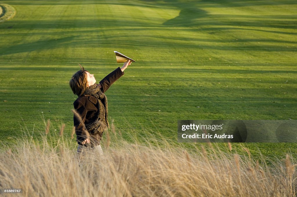 Side profile of a boy flying a paper airplane in a park