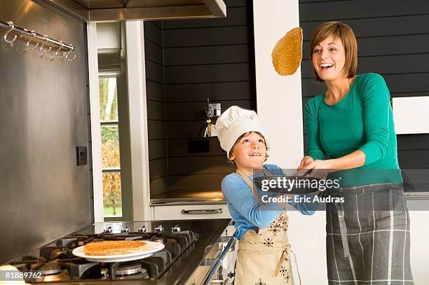 young woman flipping a pancake with her son - crêpe pancake photos et images de collection