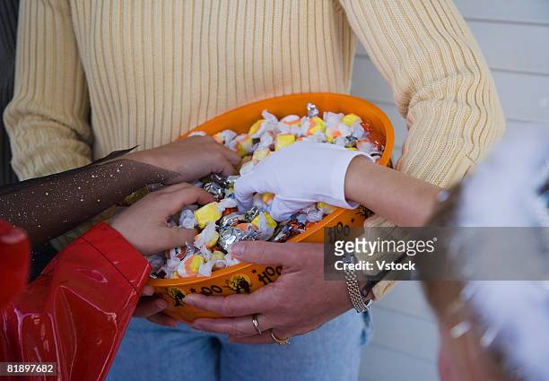 children in halloween costumes reaching into bowl of candy - bowl of candy stock-fotos und bilder