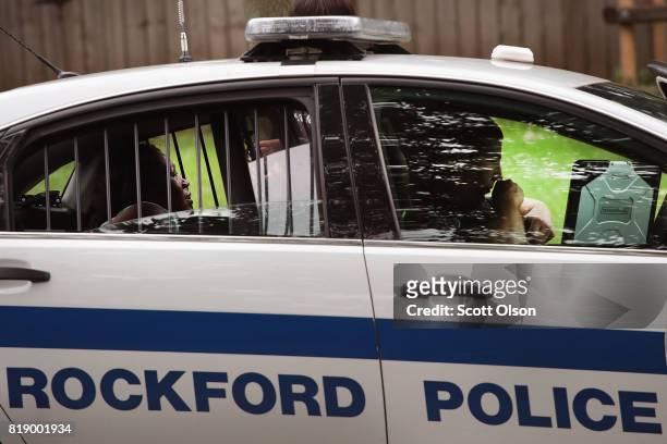 Woman sits in the back of a squad car after she was taken into custody for fighting outside of a suspected drug house on July 12, 2017 in Rockford,...