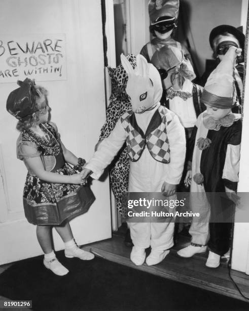 Children in costumes arriving at a Halloween party, USA, circa 1955. A sign on the door warns 'Beware Ghosts are within!'.