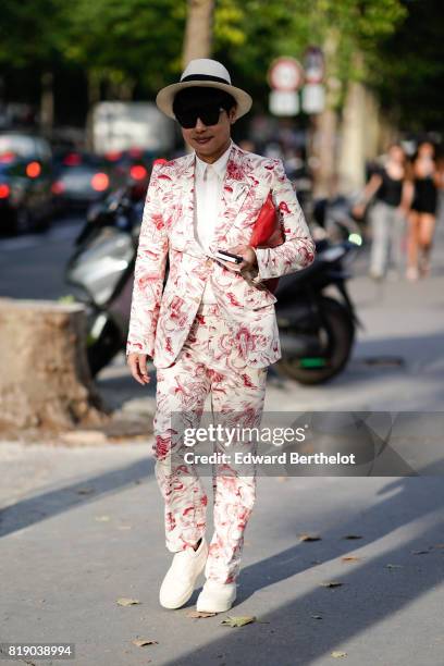 Guest wears a hat, sunglasses, a blazer jacket, suit pants, white shoes, a red clutch, outside the launch party for Chanel's new perfume 'Gabrielle',...