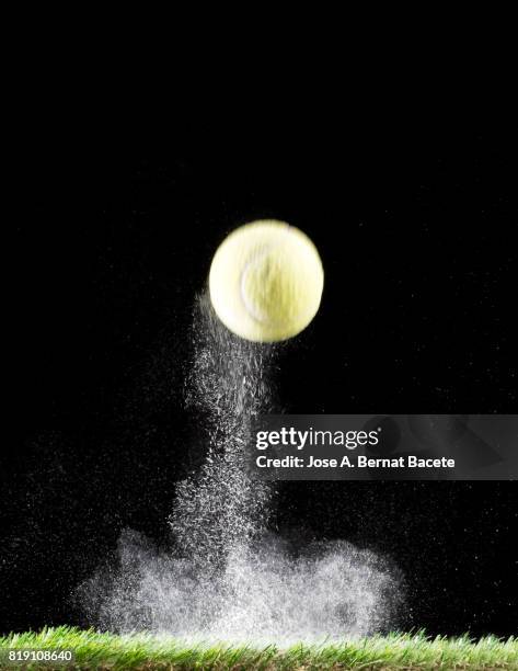 impact and rebound of a ball of tennis on a surface of grass and powder on a black background - ballon rebond stock-fotos und bilder