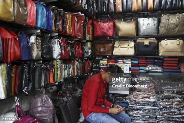 Vendor uses a mobile phone while waiting for customers at the Shakra Leather Arts store in the Dharavi area of Mumbai, India, on Tuesday, July 18,...