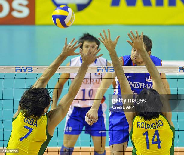 France's Jean-Philippe Sol spikes the ball against Brazil's Giba and Rodrigao during their Volleyball World League fifth round match in Belo...