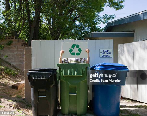 person standing behind waste bins holding recycling sign - wheelie bin stock pictures, royalty-free photos & images