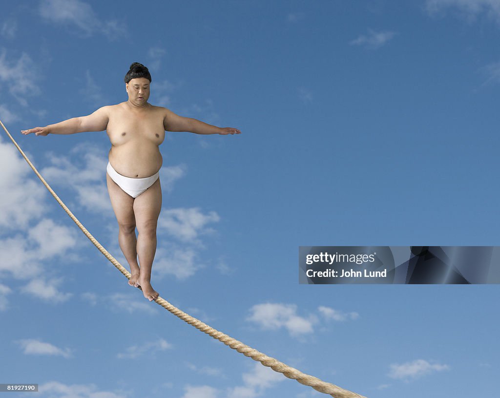 Sumo wrestler walking on a tightrope against a blue sky