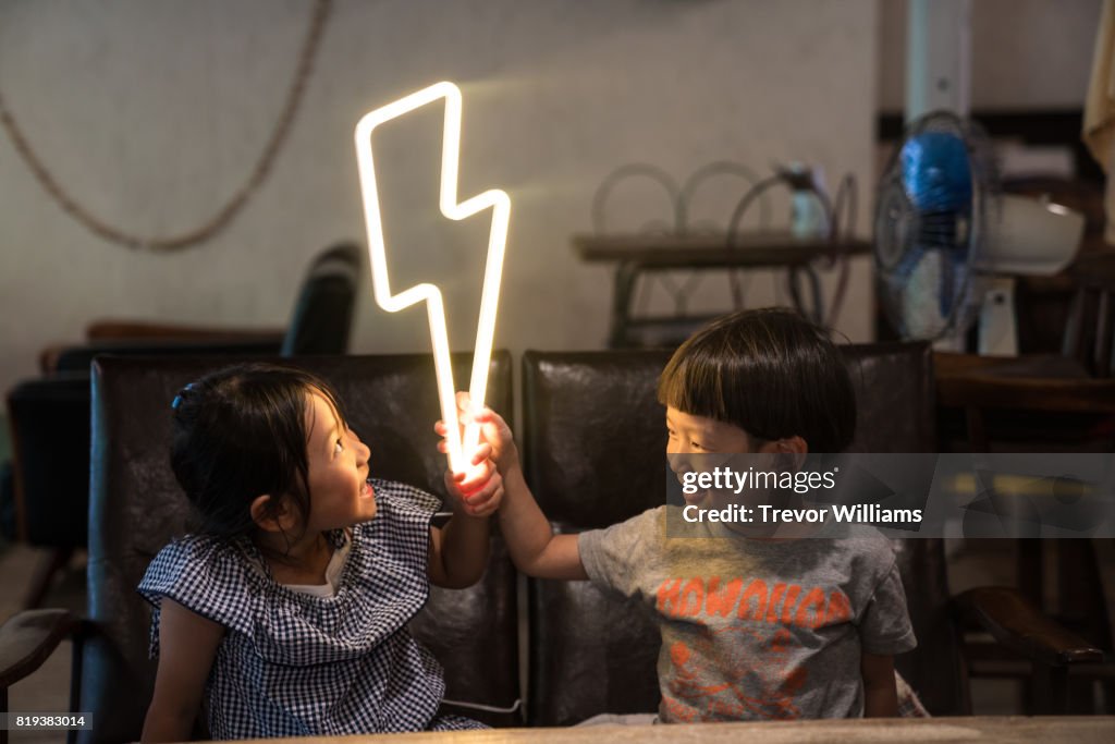 Two small children holding a lightning bolt shaped neon light