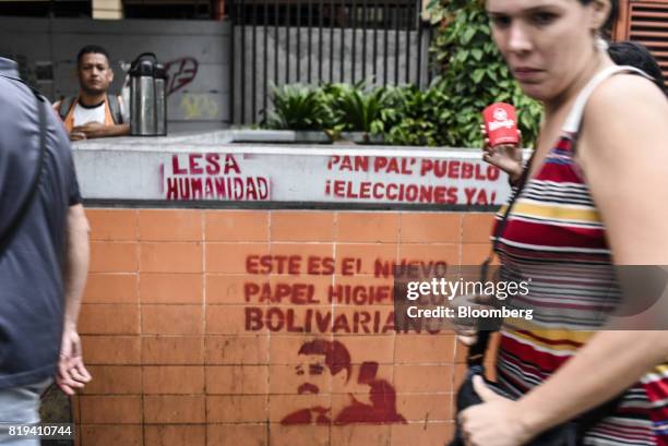 Pedestrian pass in front of graffiti with slogans against Venezuelan President Nicolas Maduro in Caracas, Venezuela, on Wednesday, July 19, 2017....