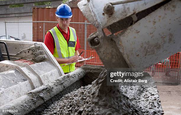 building worker watching concrete being poured from lorry - betonmischmaschine stock-fotos und bilder