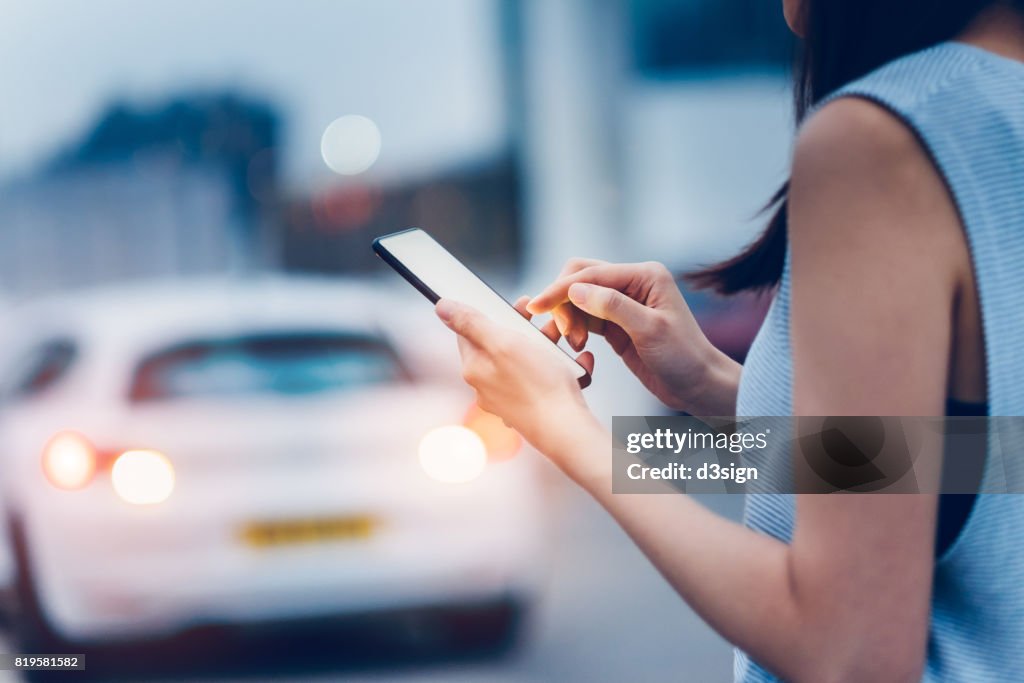 Woman using smartphone while waiting for a taxi ride on city street