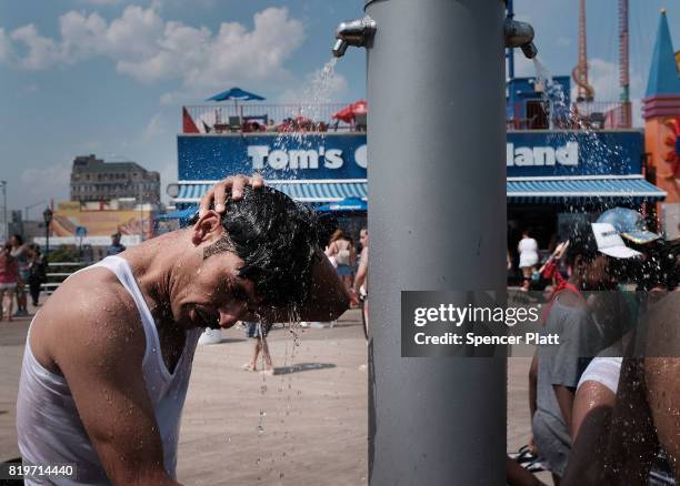 Man cools off under a shower on the boardwalk at Coney Island on July 20, 2017 in the Brooklyn borough of New York City. Throughout the region people...