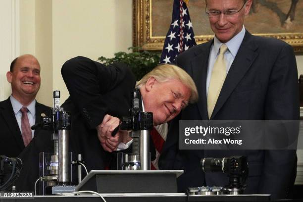 President Donald Trump tries to break a medicine bottle with a press as Corning CEO Wendell Weeks and Rep. Tom Reed look on during an announcement...